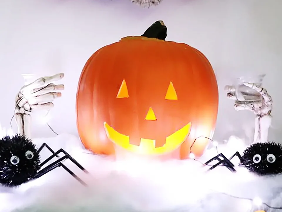 Spooky Jack-o'-lantern centerpiece with skeleton hands holding glasses and spiders.