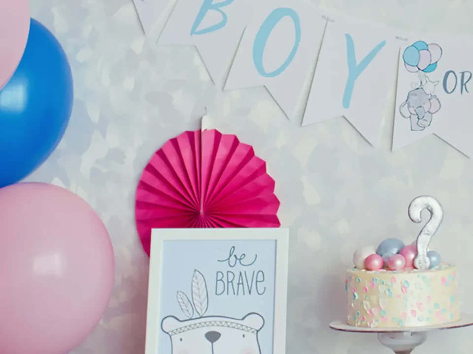 Gender reveal party decorations: cake, balloons, "Boy or...?" banner, and "Be Brave" sign.