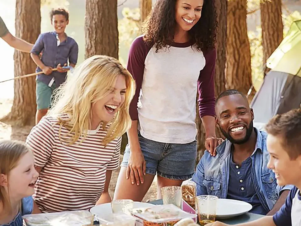 Happy family enjoys a meal at a campsite, using dry ice to keep food cold.