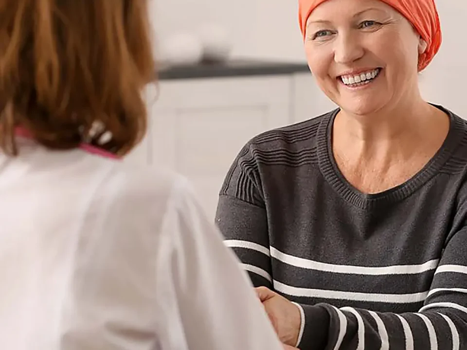 Smiling woman with cancer wearing a chemo cold cap, talking with her doctor.