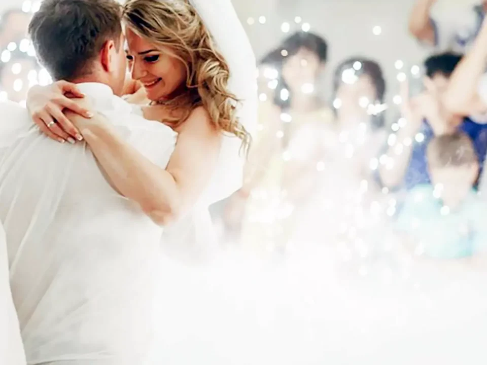 Happy bride and groom embrace during their first dance, surrounded by sparkling dry ice effects.