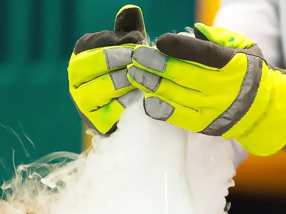 Hands in safety gloves handling dry ice, producing vapor. Dry ice safety.