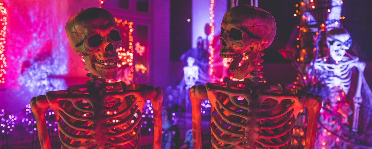 Two skeletons illuminated by purple and red Halloween lights.