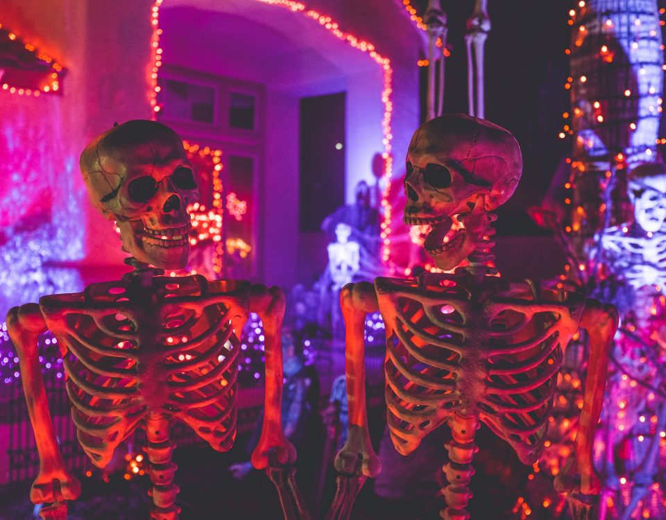 Two skeletons illuminated by purple and red Halloween lights.