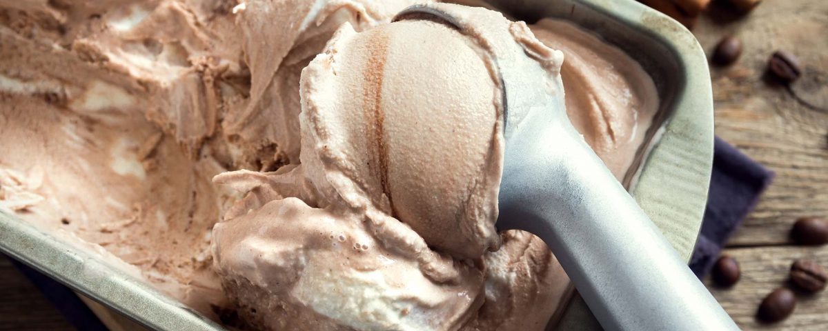 An ice cream scoop is used to scoop chocolate ice cream from a metal container.