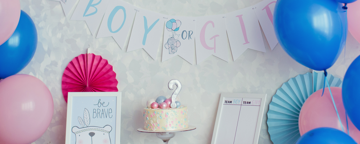 A "Boy or Girl?" sign hangs on the wall behind a cake and festive decor for a gender reveal party